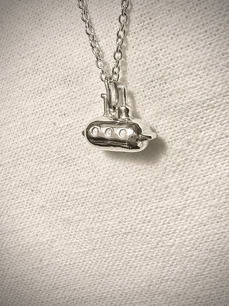 Silver submarine pendant on a chain against a textured beige background