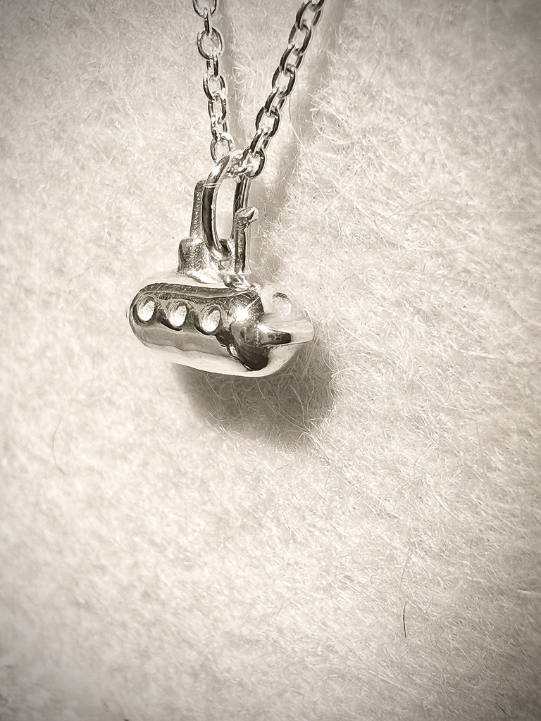 Silver pendant necklace of a little submarine 
on a textured gray background