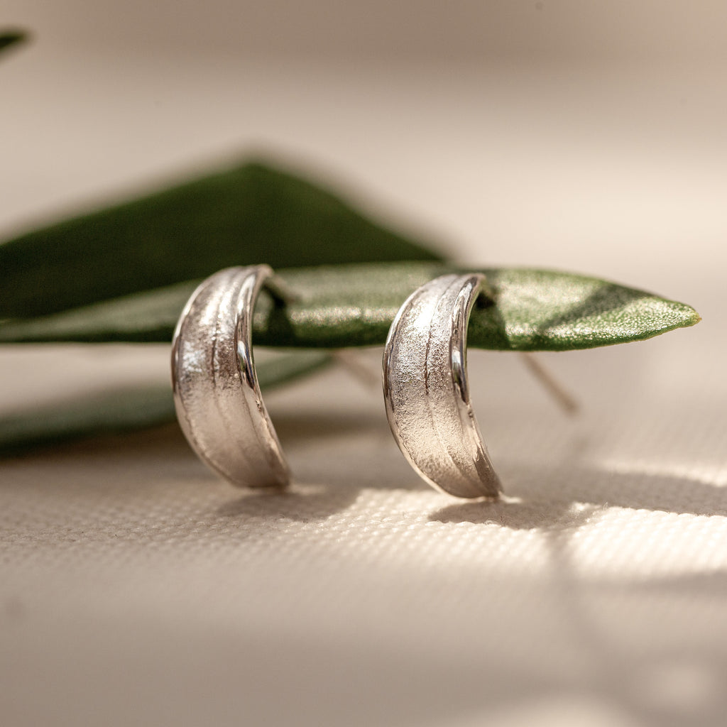 Sterling silver olive leaf huggie stud earrings on olive leaf.
