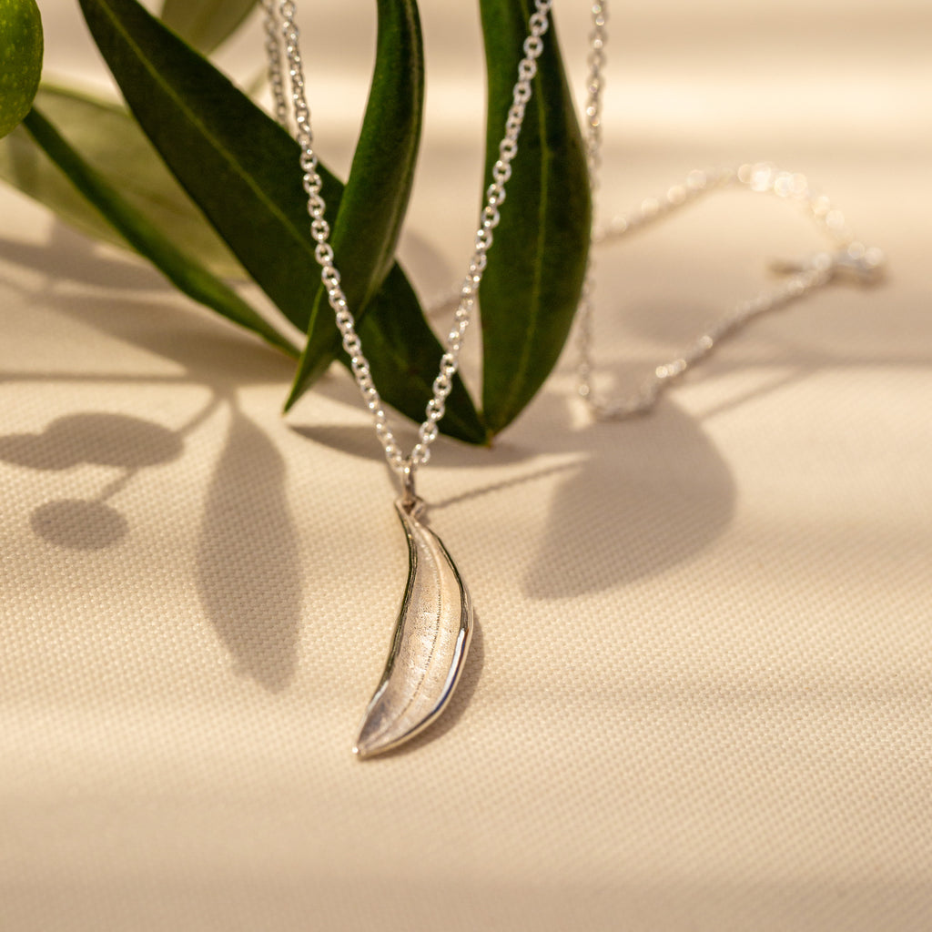 Sterling silver olive leaf pendant on cable chain with olive leaves in background.
