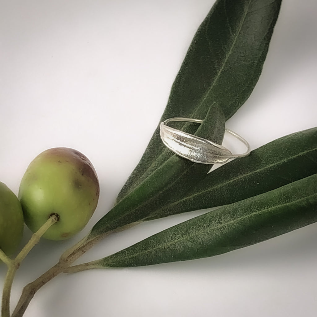 Sterling silver handmade dainty olive leaf ring resting on olive leaves.