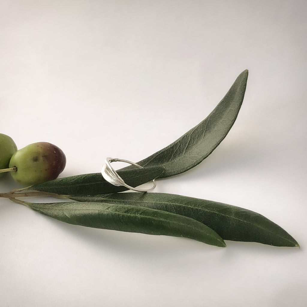 Handmade sterling silver dainty olive leaf ring resting on olive leaves.