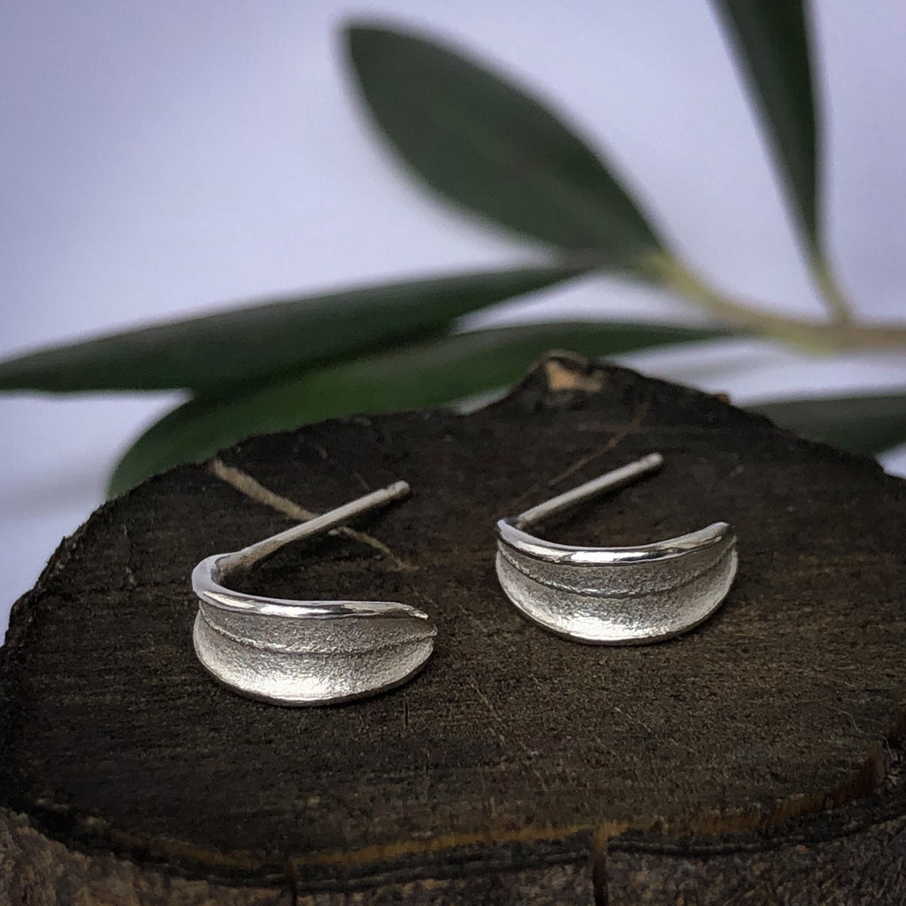 Sterling silver olive leaf huggie stud earrings on olive wood.