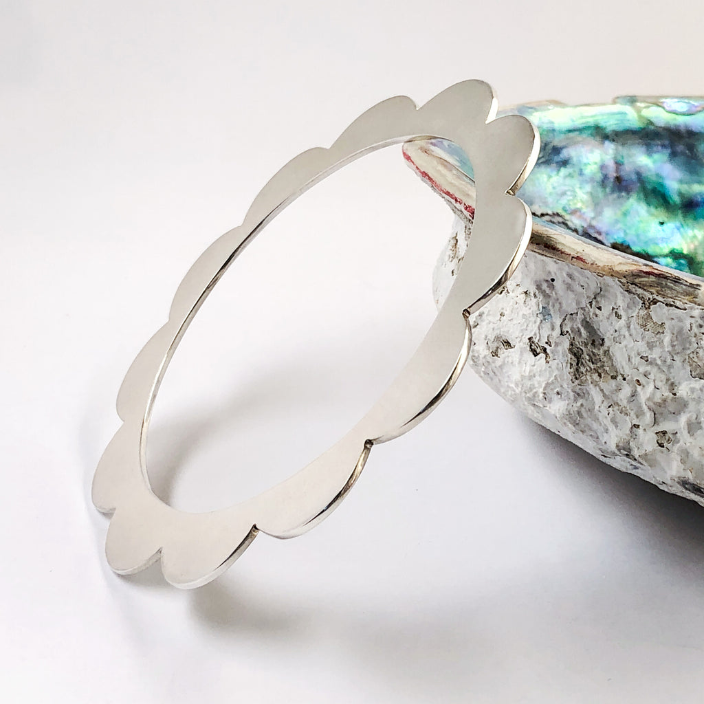 Sterling silver bangle with scalloped edges resting on paua shell.
