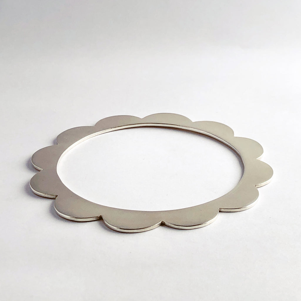 Sterling silver bangle with scalloped edges on white background.