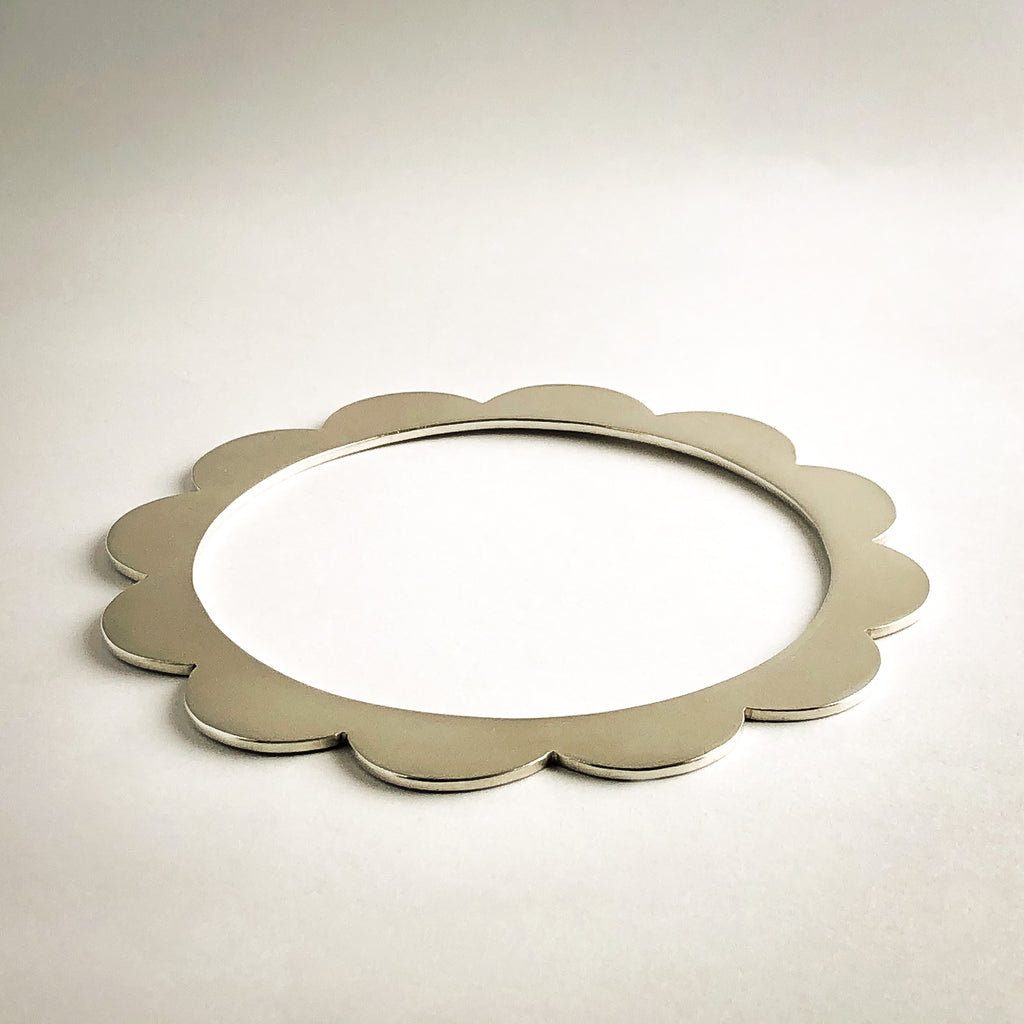 Sterling silver bangle with scalloped edges with white background.