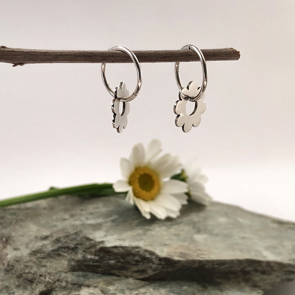 Sterling silver around earring withscalloped edges  swinging freely through the centre hole on a sterling silver sleeper with daisy on rock in background.