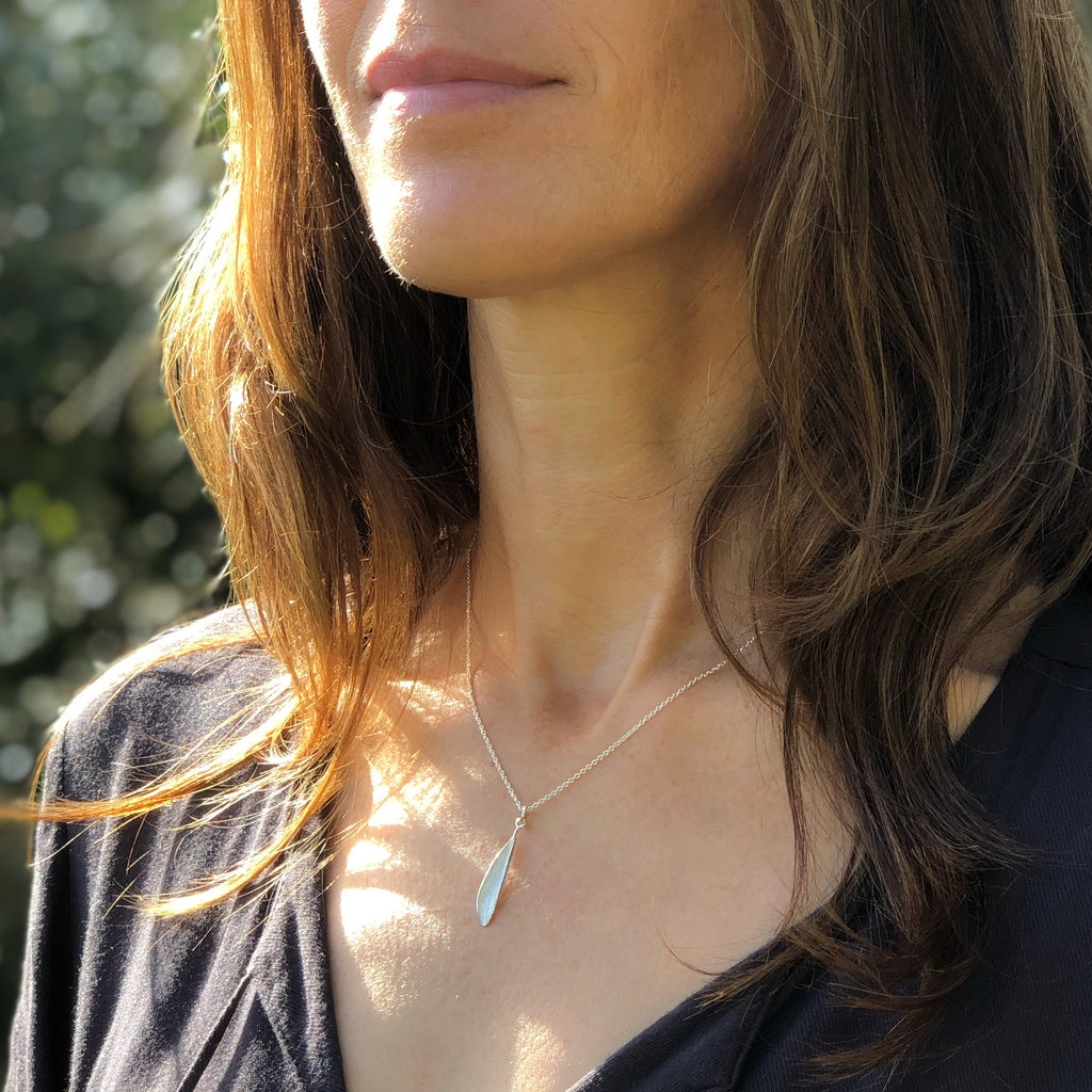 Model wearing handmade sterling silver Picual olive leaf pendant that hangs on a fine sterling silver chain.
