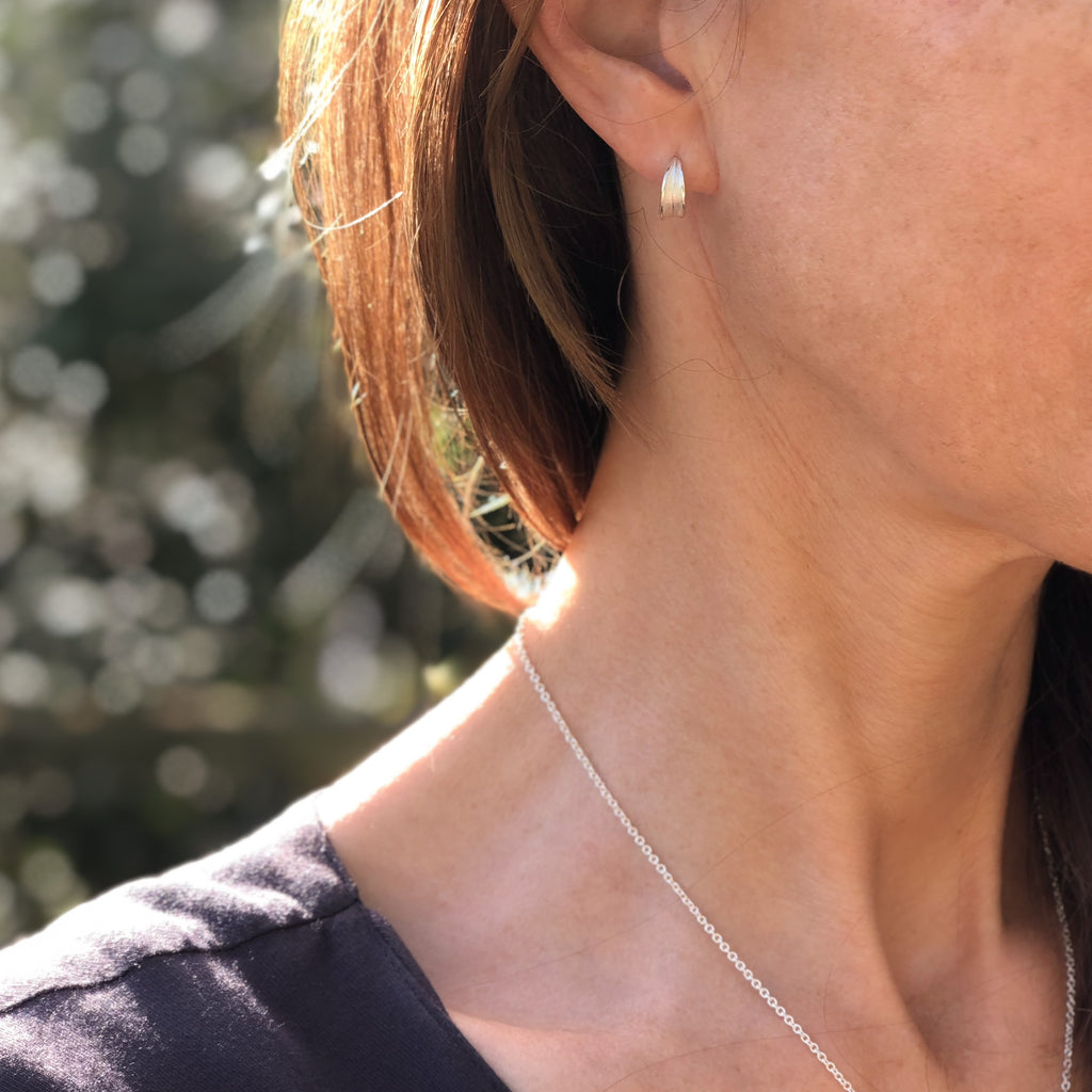Close up of model wearing sterling silver olive leaf huggie stud earrings.