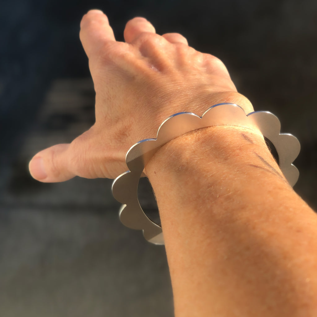 Woman's wrist wearing Sterling silver bangle with scalloped edges.