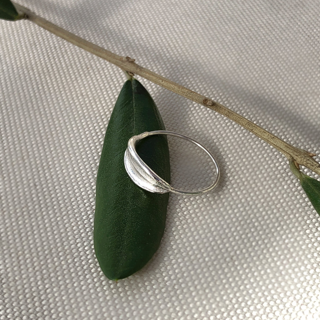 Handmade sterling silver dainty olive leaf ring resting on olive leaves.