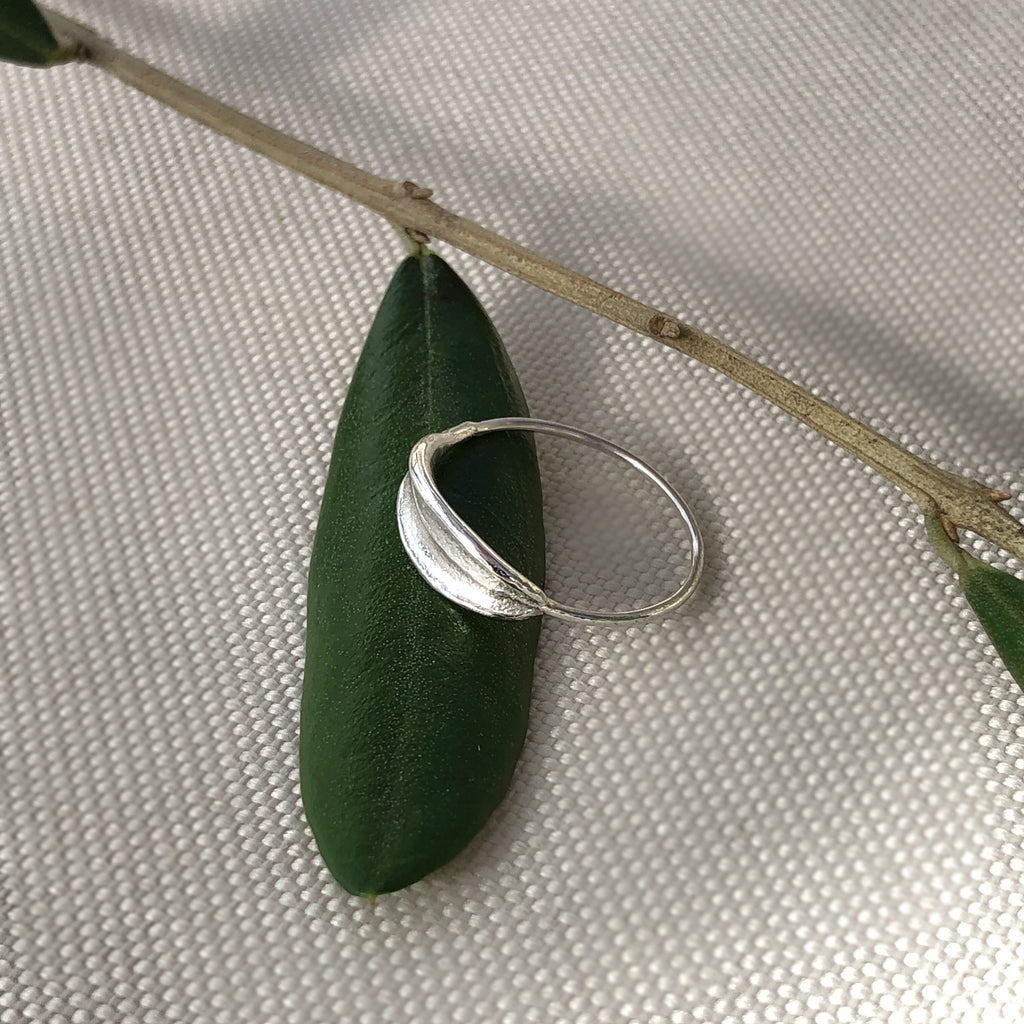 Sterling silver dainty olive leaf ring resting on olive leaves.
