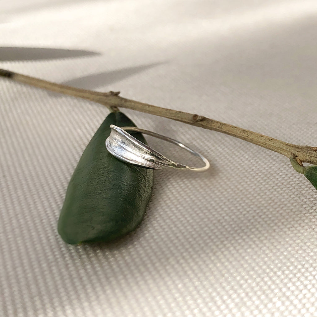 Handmade sterling silver dainty olive leaf ring resting on olive leaves.